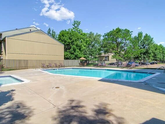 Charming pool area in a tranquil apartment complex, surrounded by lush greenery and sunny skies, offering a perfect retreat.