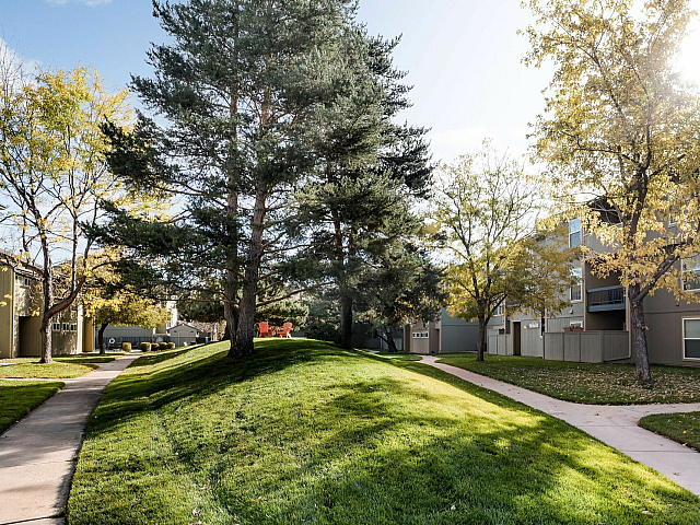 Beautiful apartment community surrounded by lush green lawns, mature trees, and a tranquil pathway, offering serene outdoor living.