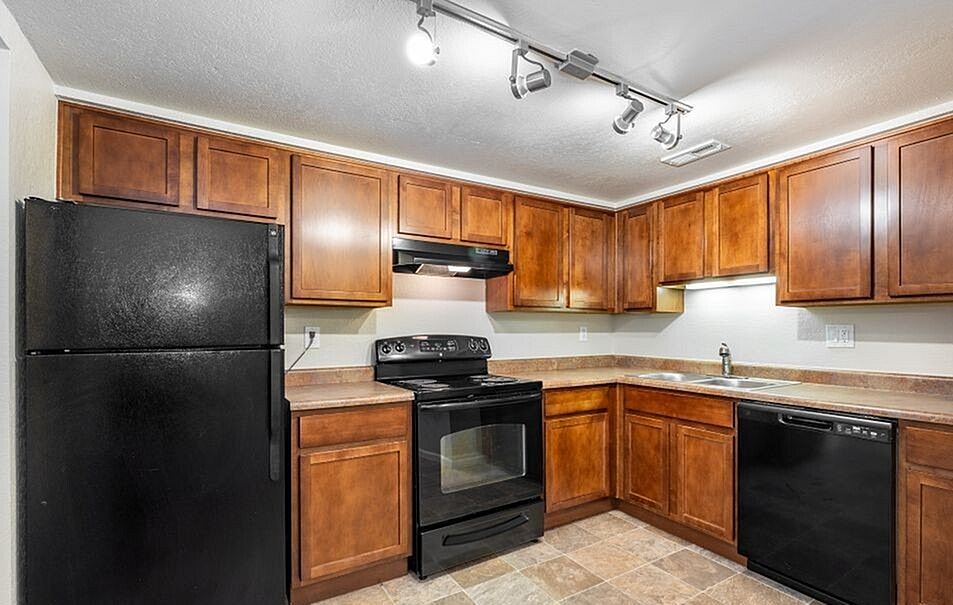 Modern kitchen with rich wooden cabinets, sleek black appliances, and track lighting, perfect for culinary enthusiasts.