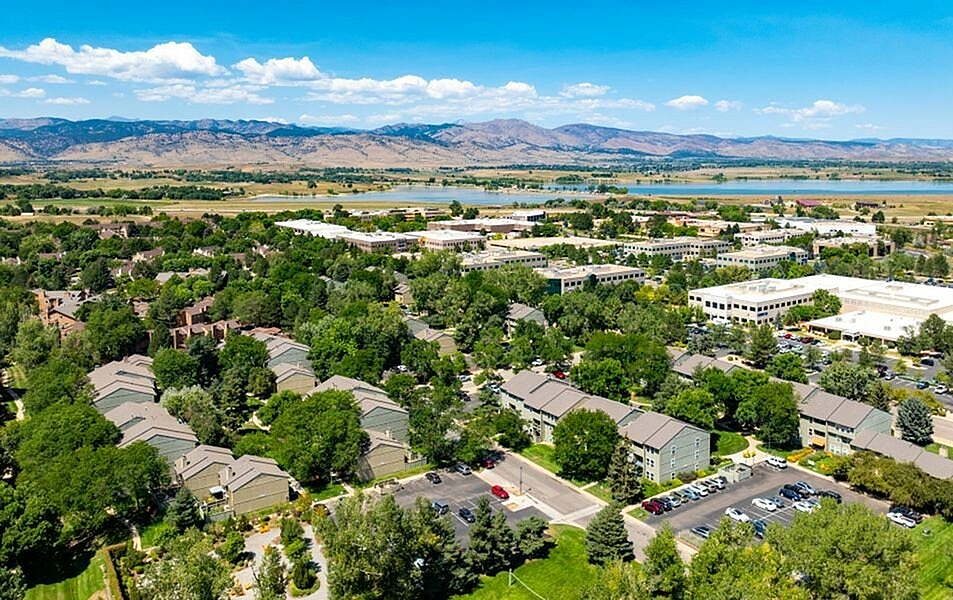 Beautiful aerial view of a serene residential area surrounded by lush greenery and distant mountains under a clear blue sky.