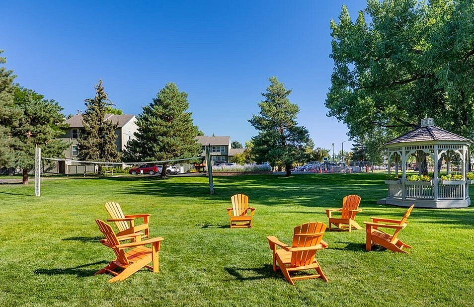 Charming outdoor space with vibrant Adirondack chairs encircling an elegant gazebo, surrounded by lush greenery and mature trees.