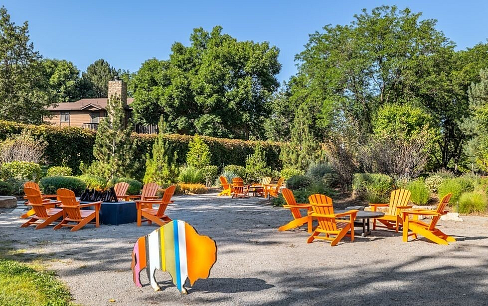 Charming outdoor seating area with vibrant orange chairs and a colorful buffalo sculpture, surrounded by lush greenery and peaceful natural ambiance.