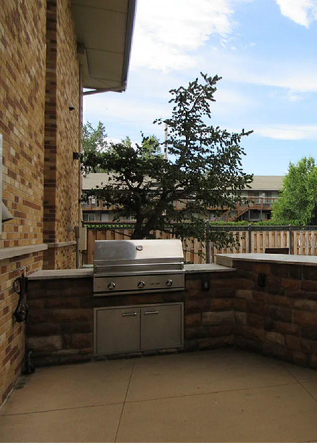 Charming outdoor patio featuring a built-in BBQ grill and cozy seating area, perfect for entertaining under a blue sky.