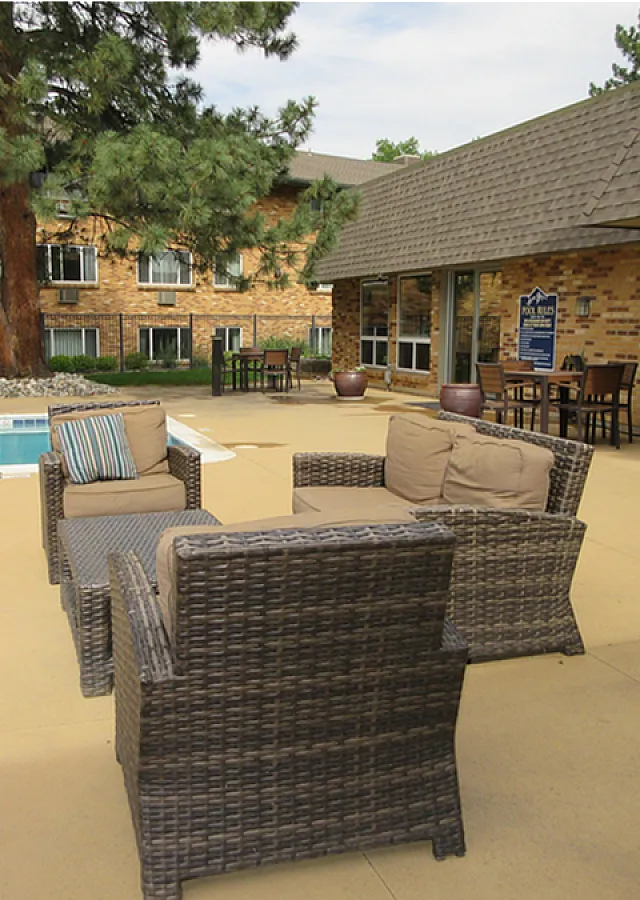 Inviting outdoor patio with cozy wicker seating overlooking a serene pool, surrounded by lush greenery and charming brick architecture.