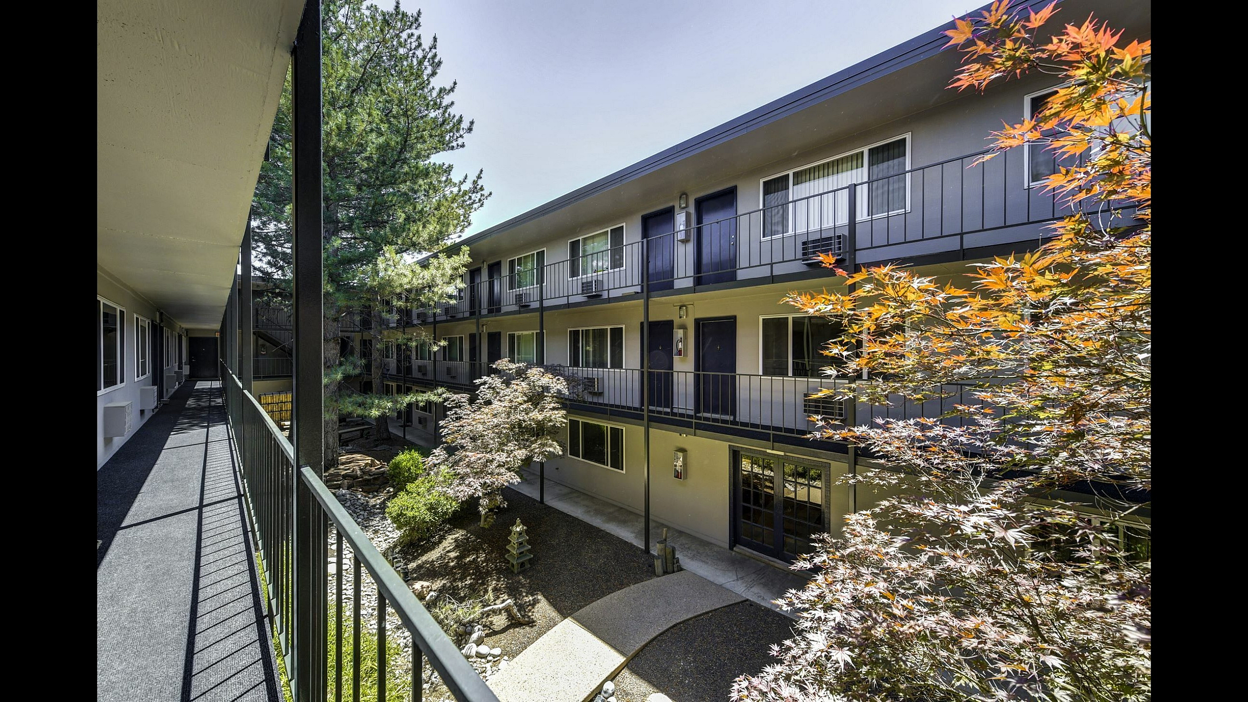 Charming apartment complex with lush courtyard garden, modern railings, and sunlit walkways.