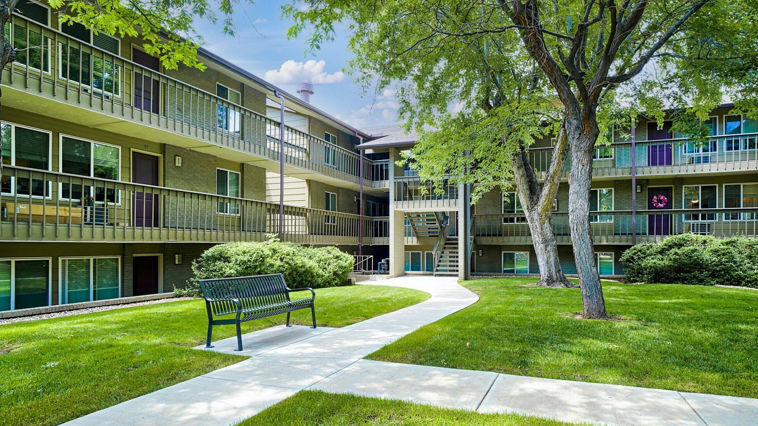 Scenic apartment complex exterior with lush green courtyard and mature trees, offering serene living environment.