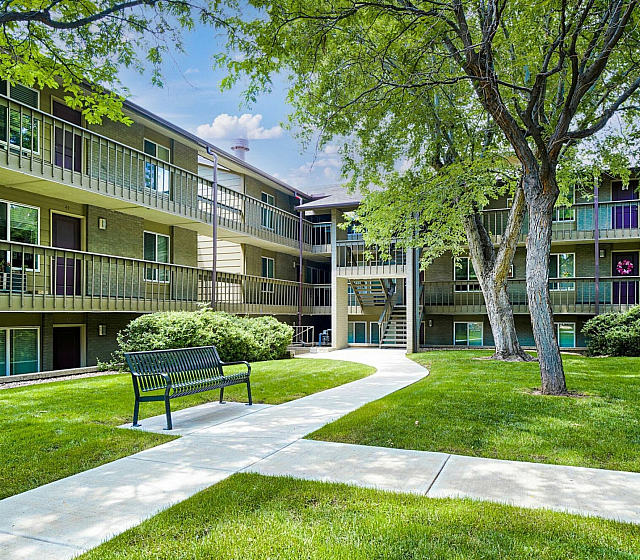 Charming apartment complex with lush green landscaping, mature trees, and a welcoming walkway, highlighting tranquil suburban living.
