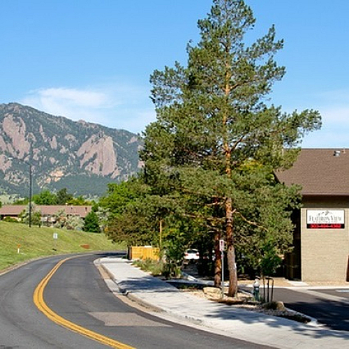 Charming apartment complex nestled against scenic mountain backdrop, featuring lush greenery and a serene road view.