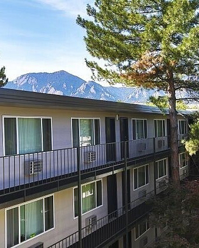 Charming apartment building nestled among lush trees with stunning mountain views, offering serene living and natural beauty.