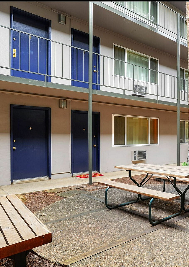 Inviting apartment courtyard featuring modern design with blue doors, surrounded by lush greenery and serene outdoor seating.