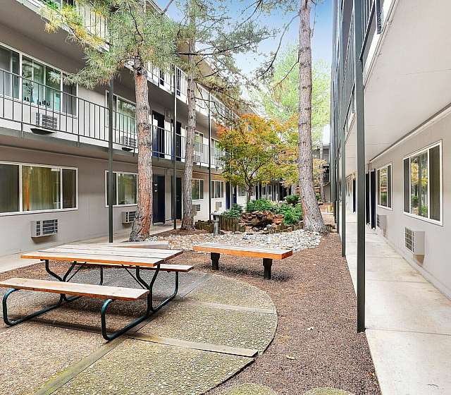 Charming courtyard view of a modern apartment complex with lush trees, tranquil rock garden, and inviting outdoor seating area.