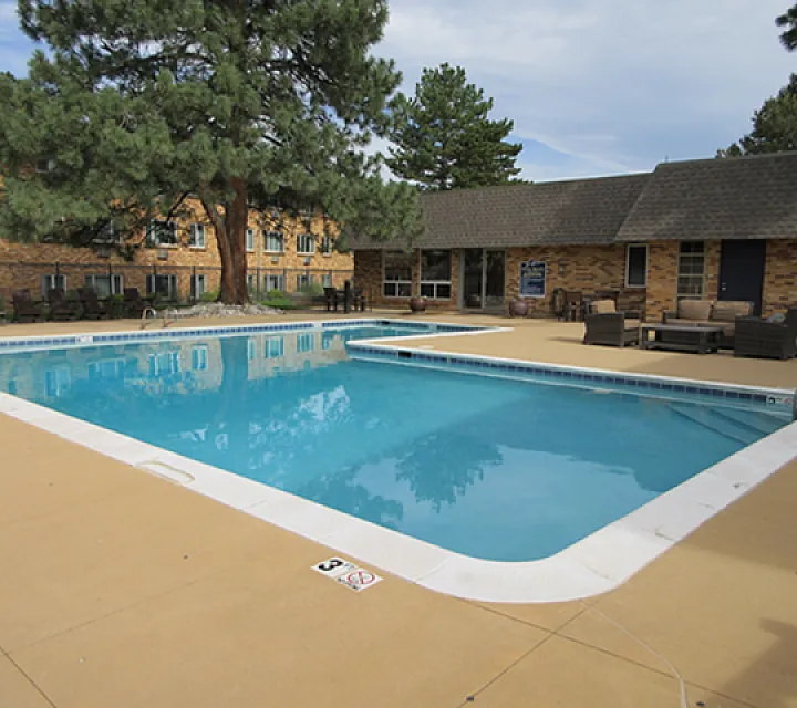 Inviting outdoor pool area surrounded by lush greenery, comfortable seating, and charming brick architecture.