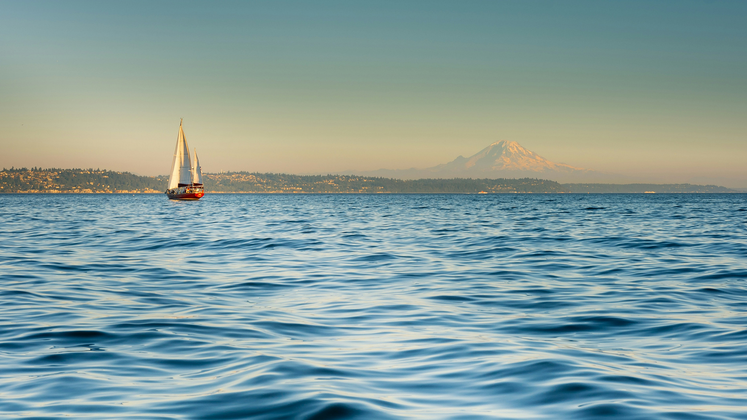 Scenic view of a sailboat gliding across tranquil waters with a majestic mountain backdrop, offering serene coastal living.