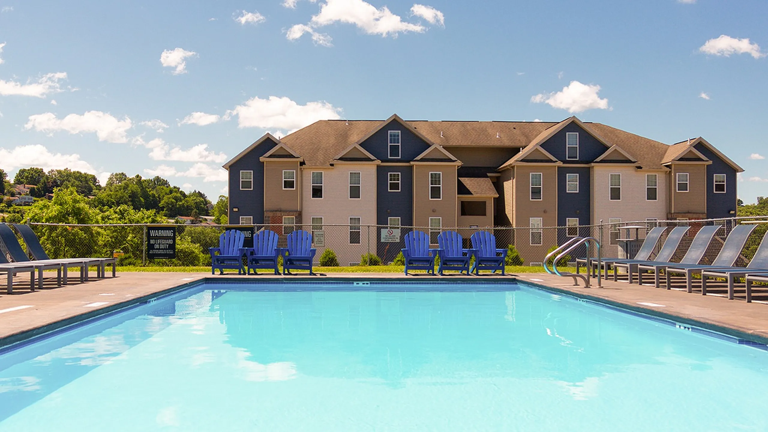Inviting apartment complex exterior showcasing a sparkling pool surrounded by lounge chairs under a bright blue sky.