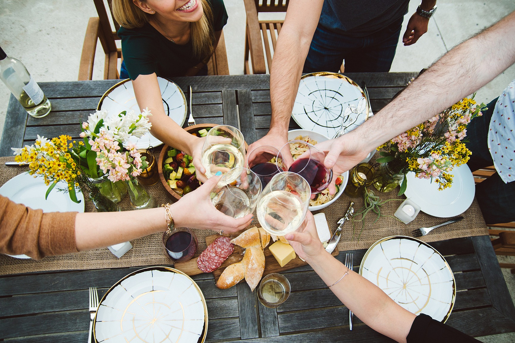 Friends toasting with wine glasses over an outdoor dinner table with flowers and food.