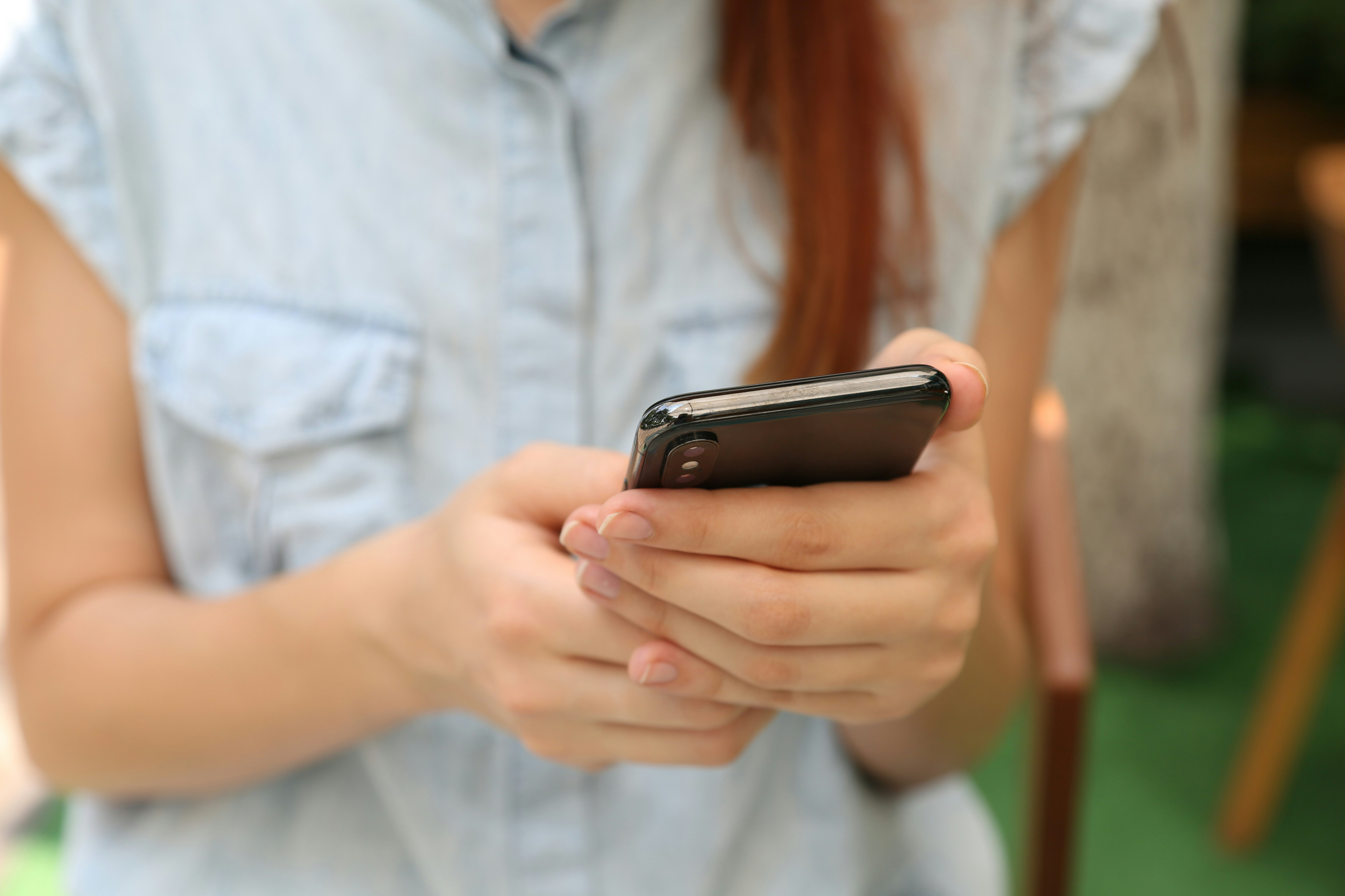 Close-up of a person using a smartphone, wearing a sleeveless denim shirt.