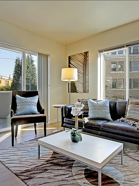 Bright and modern apartment living room with large windows and sliding glass doors, black leather couch, armchair, coffee table, and balcony access.