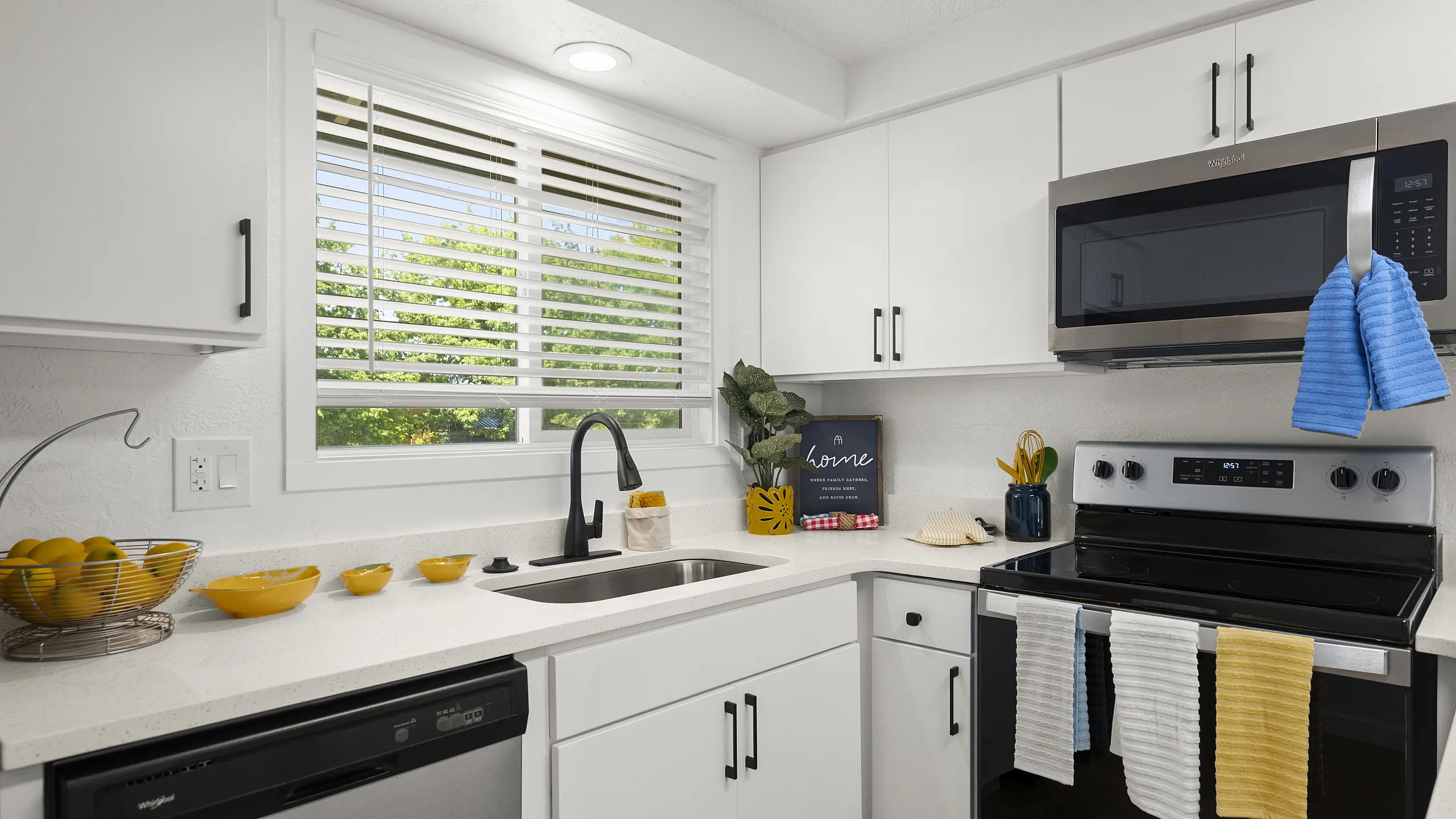 Modern kitchen with white cabinets, stainless steel appliances, black faucet, and colorful towels hanging on the oven.