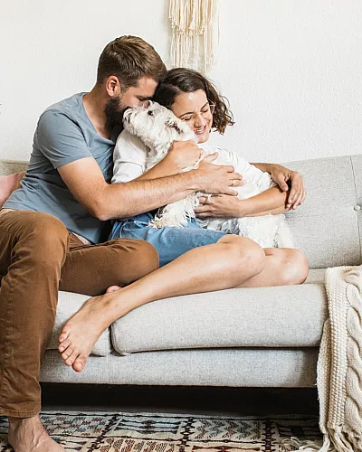 Couple sitting on a couch hugging their small white dog, creating a warm and cozy moment at home.