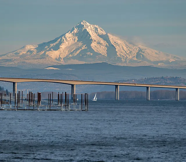 Snow-capped Mount Hood with a bridge and sailboat on the Columbia River in the foreground.