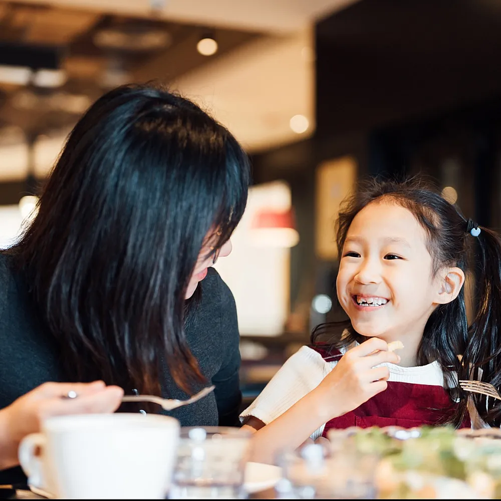 Parent and child smiling and sharing a meal together in a cozy restaurant setting.