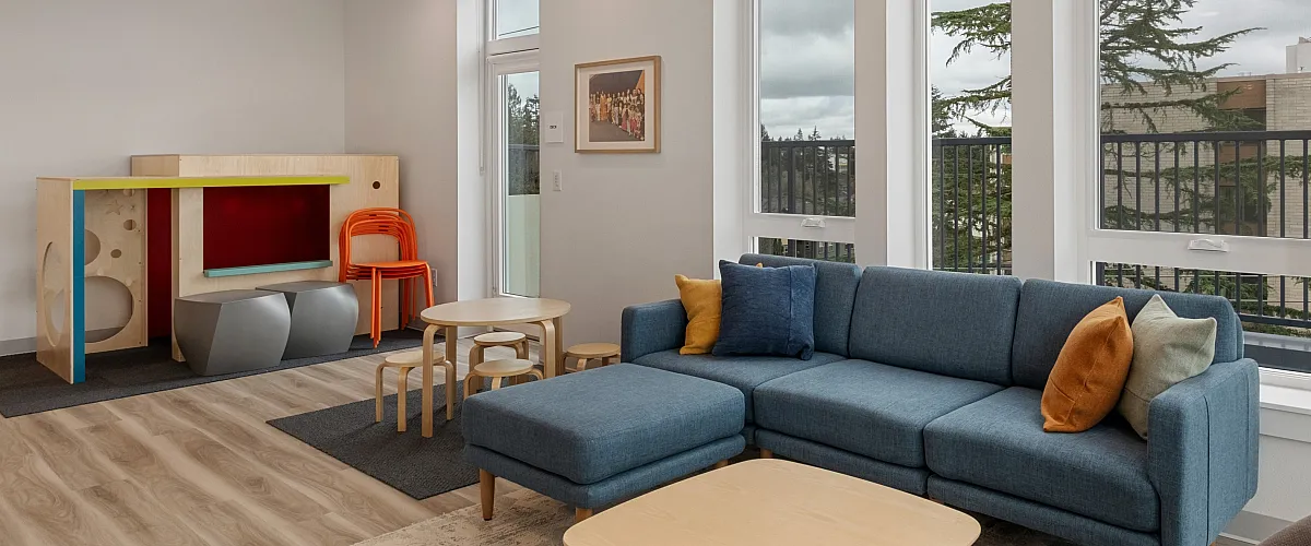 Community lounge at The Nook at Northaven featuring a children&rsquo;s play area, modern furniture, and large windows with natural light.