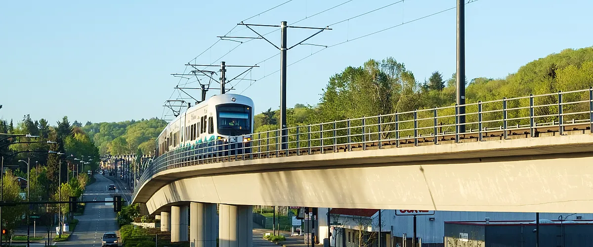 Sound Transit Link light rail traveling along an elevated track surrounded by trees and city streets in Seattle.