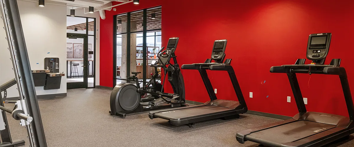 Apartment fitness center with treadmills, an exercise bike, and a bright red accent wall