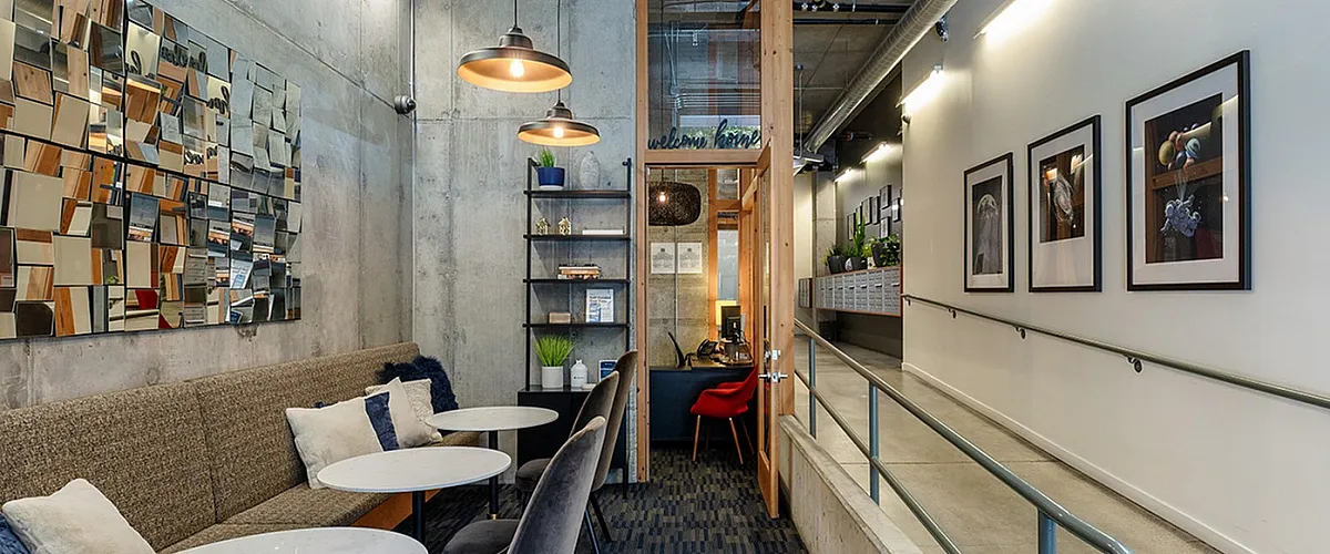 Cozy lobby space with modern lounge seating, decorative wall art, pendant lighting, and a hallway ramp leading to the mail area and office.
