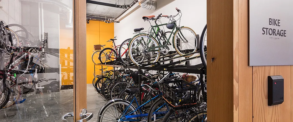 Secure indoor bike storage room with tiered racks filled with bicycles, visible through a glass door marked &ldquo;Bike Storage.&rdquo;