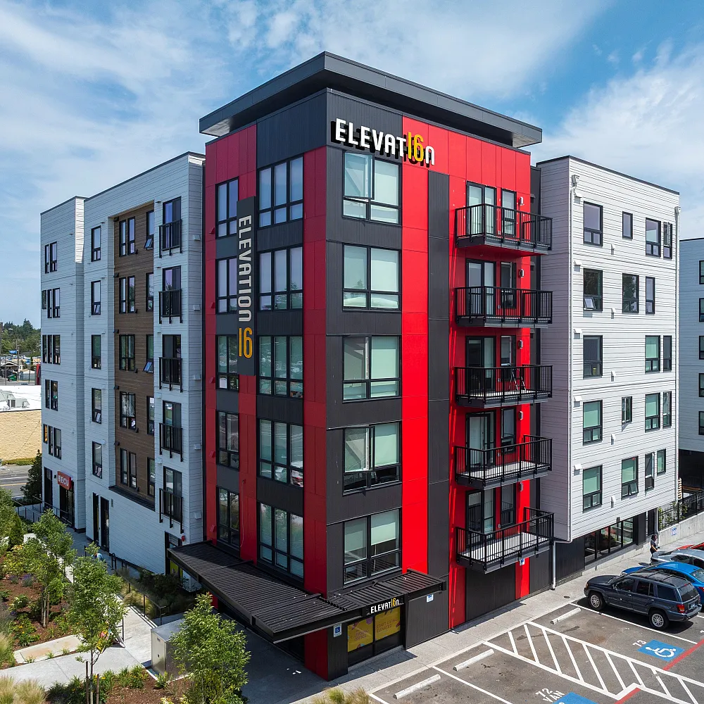 Aerial view of a modern mid-rise apartment building with white siding, large windows, and ground-level parking.