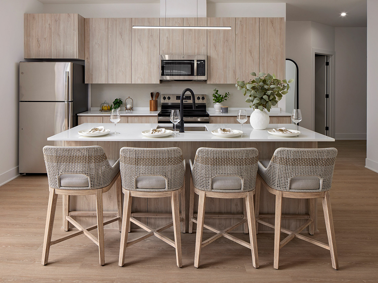 Modern kitchen with elegant wooden cabinetry, sleek stainless steel appliances, and a chic breakfast bar adorned with contemporary woven chairs.