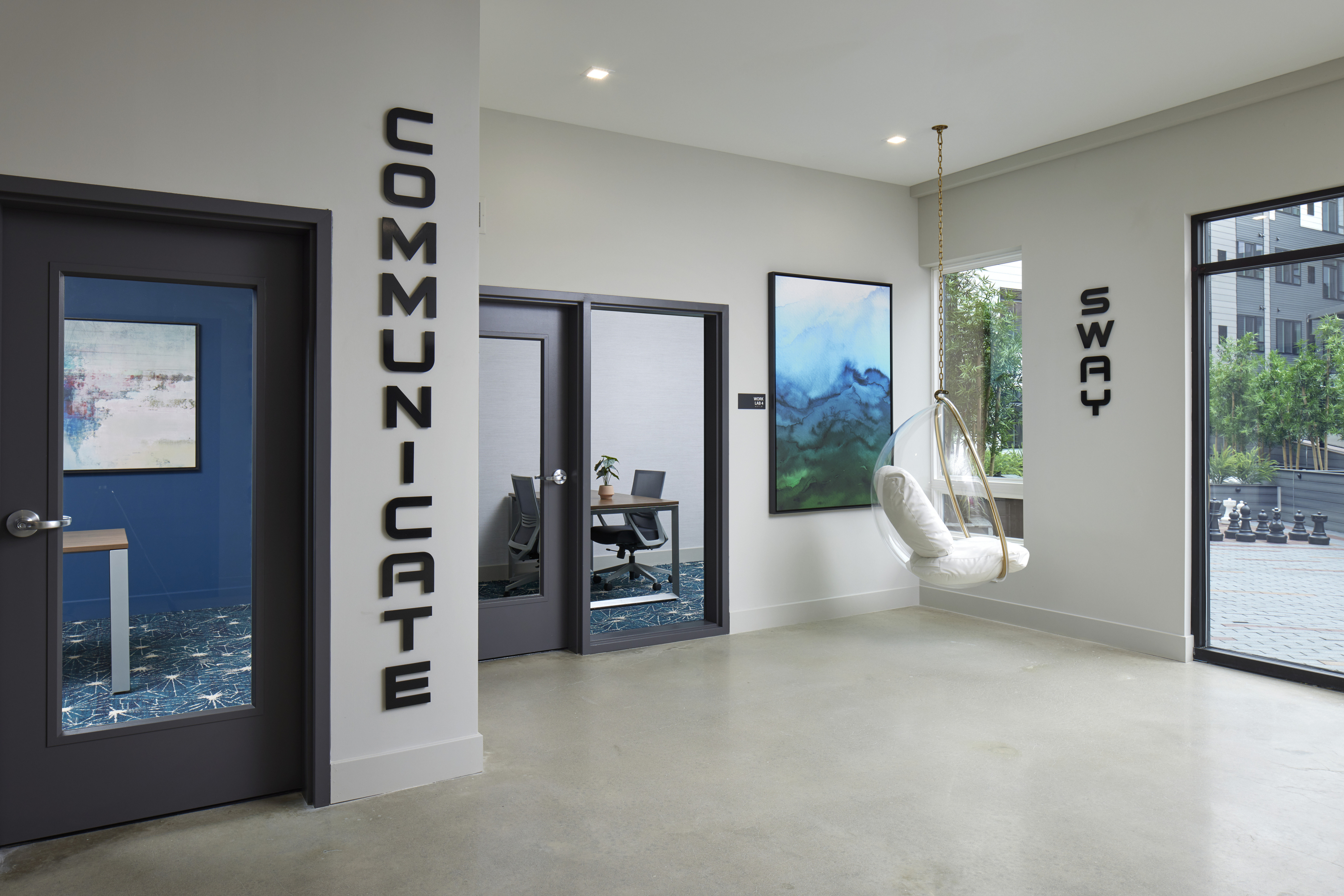 Lounge with private offices, a hanging bubble chair, abstract art, and large windows with a view of the courtyard