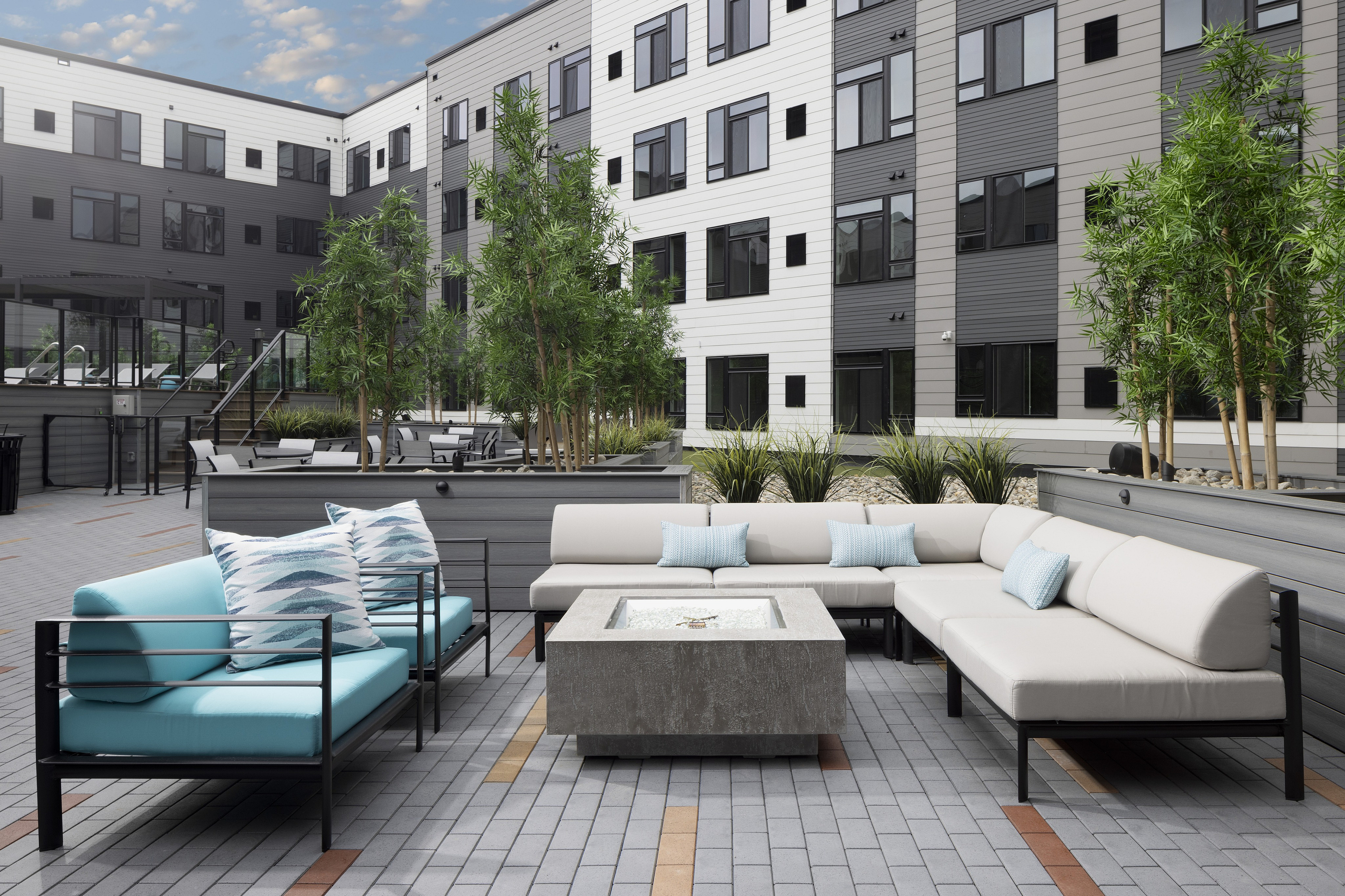 Modern apartment courtyard with stylish outdoor seating, lush greenery, and trendy brick flooring, perfect for relaxation and social gatherings.