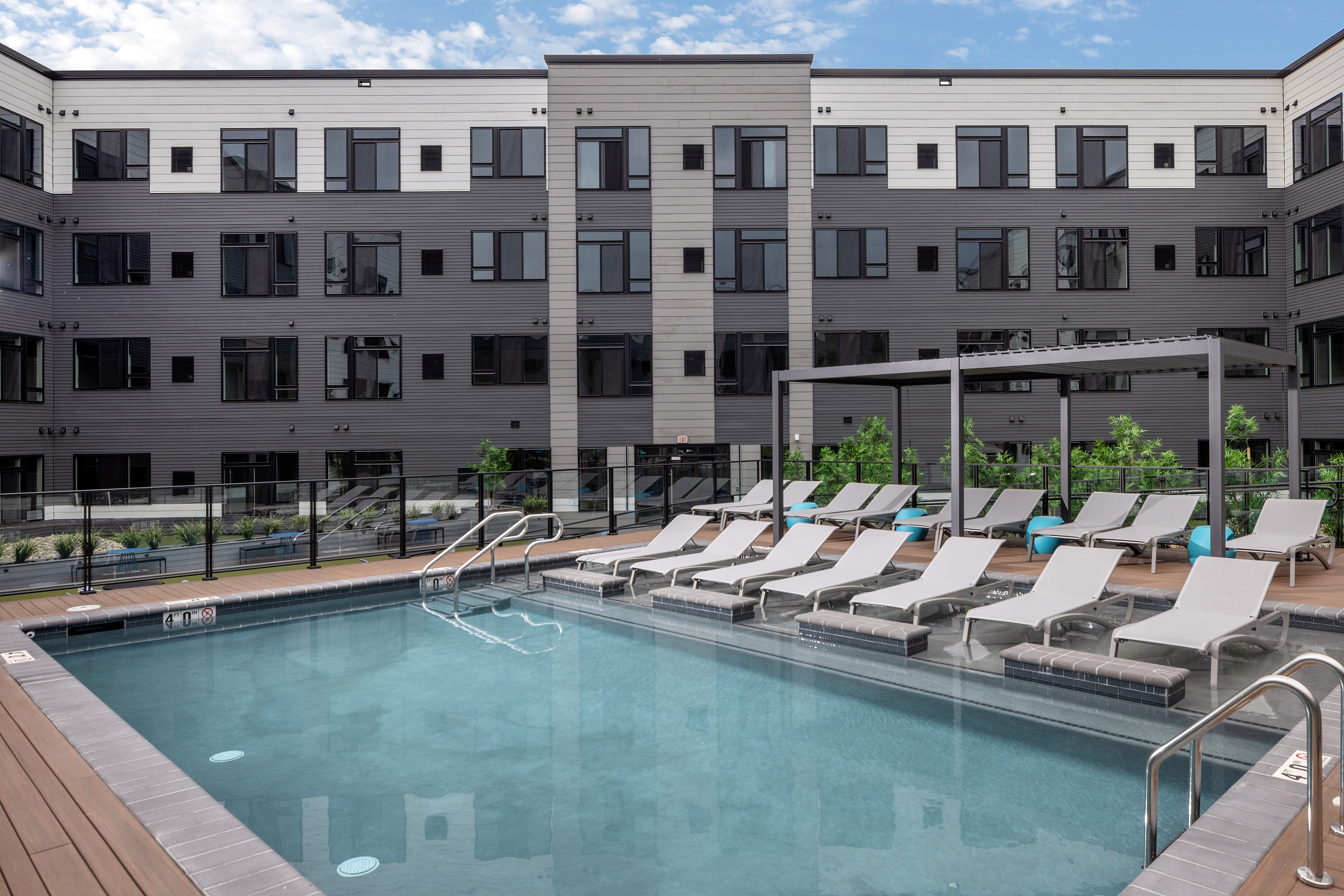 Contemporary apartment complex with a luxurious outdoor pool area featuring stylish lounge chairs and a pergola, perfect for relaxation and leisure.