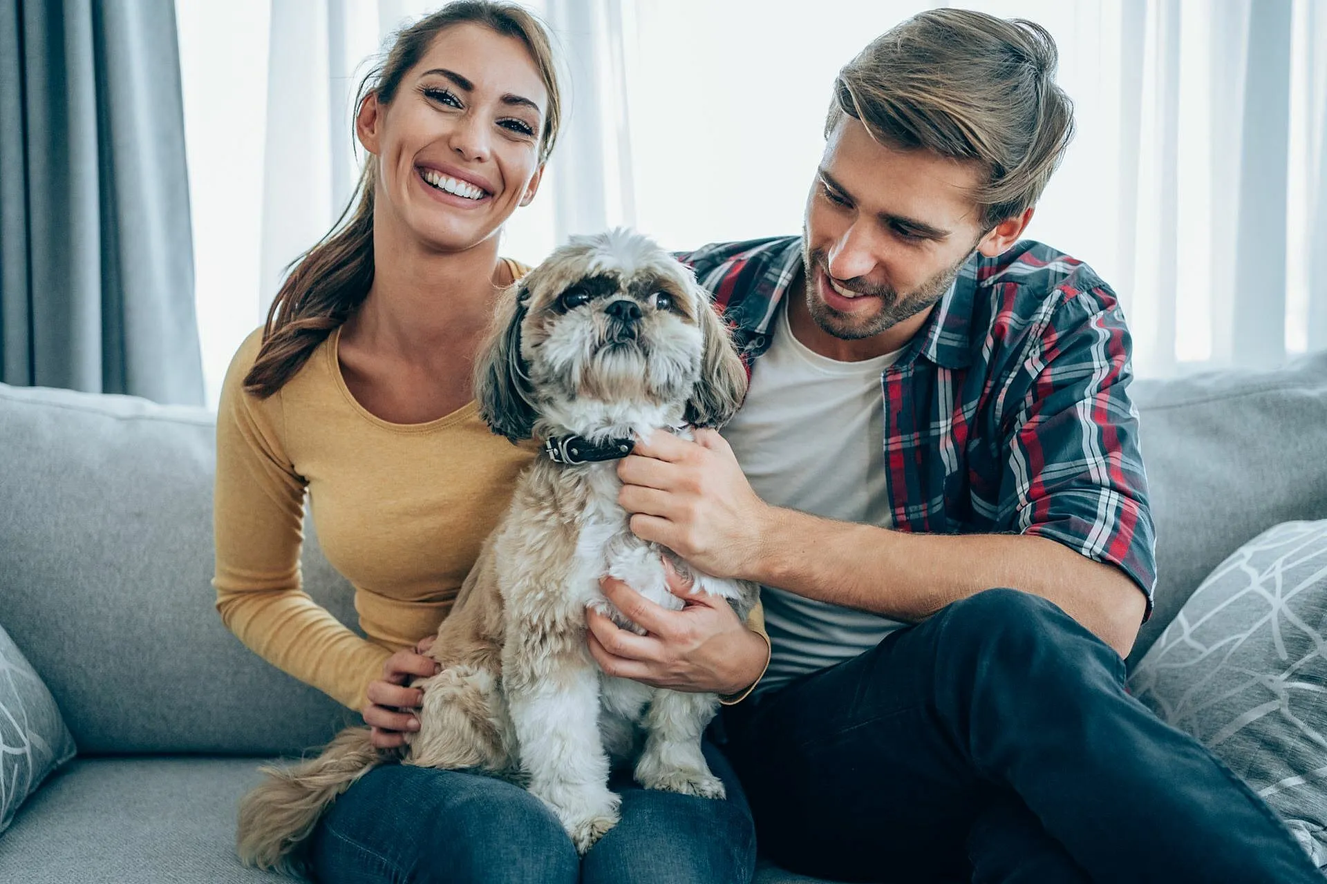 Happy couple sitting on a cozy sofa in a bright living room with their adorable dog, enjoying a relaxed and joyful atmosphere.