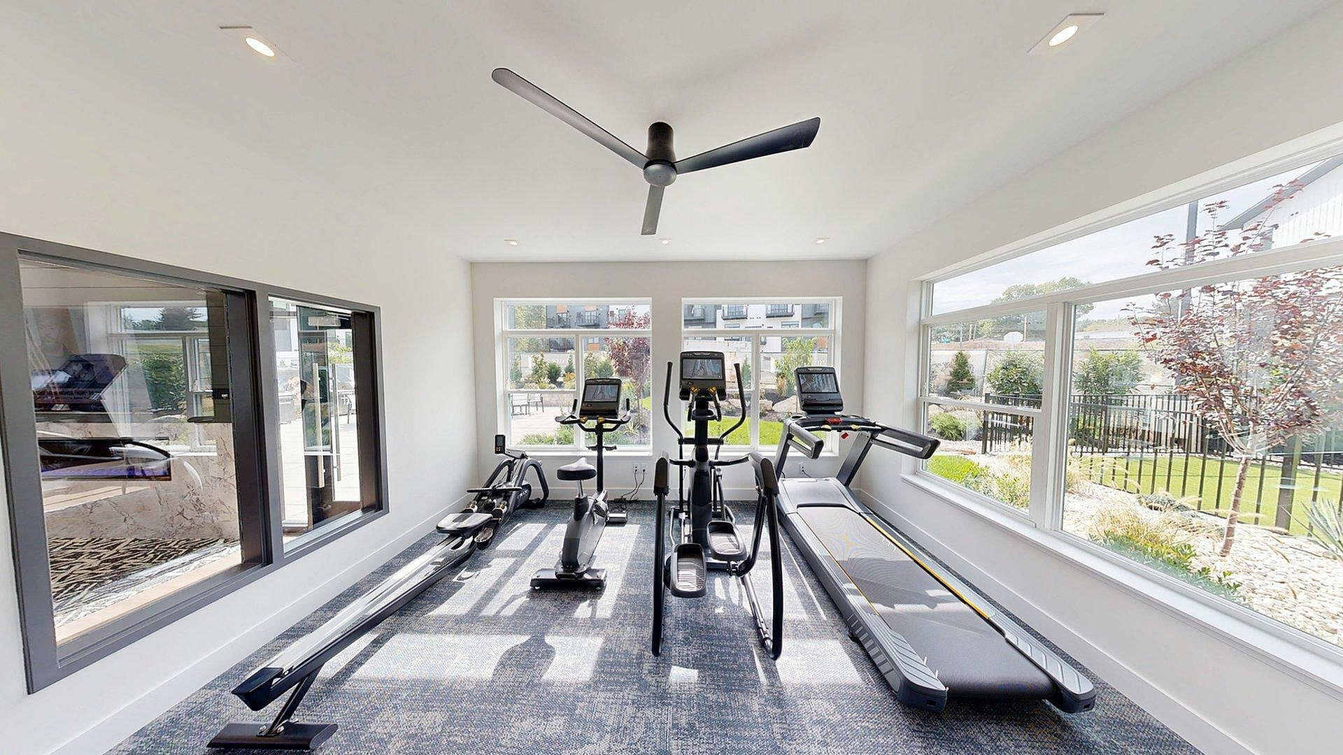 Bright and modern gym room with sleek exercise equipment and large windows offering a picturesque garden view.