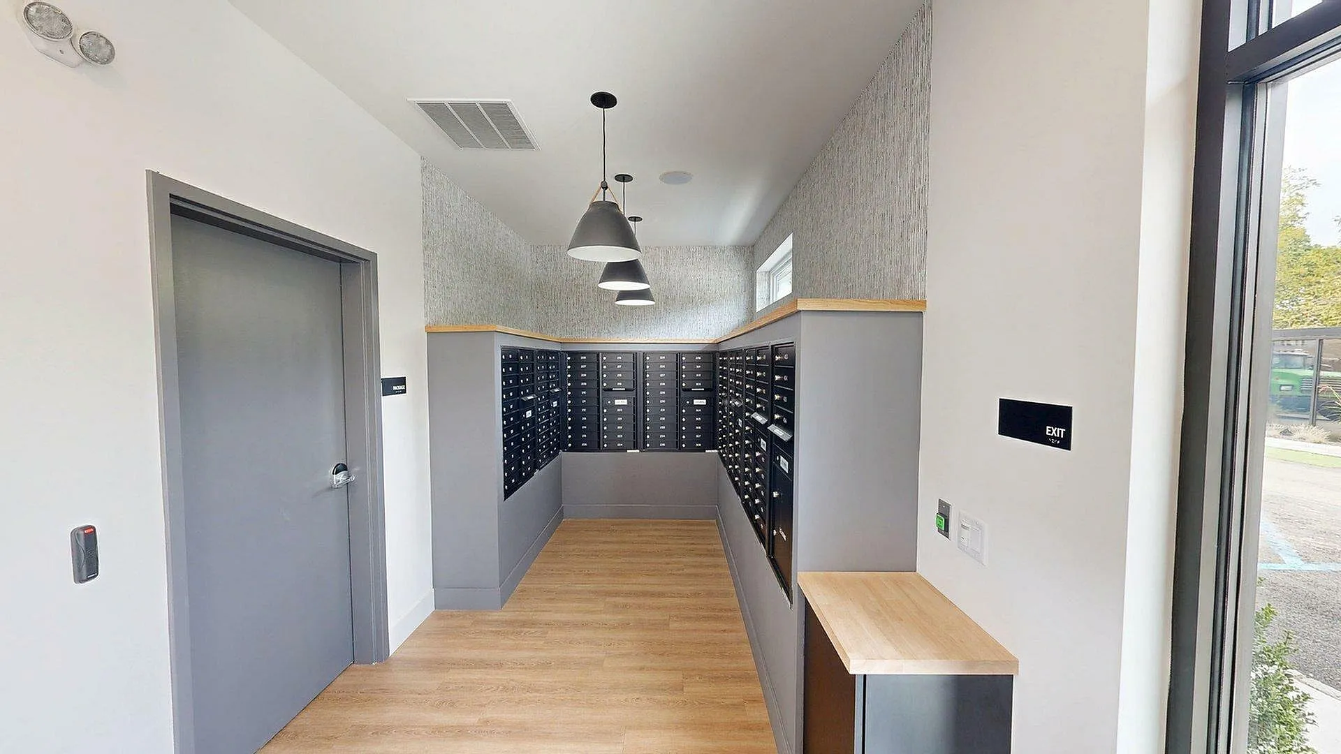Modern mailroom with sleek gray lockers, wooden flooring, and stylish pendant lighting, offering a secure and efficient mail retrieval experience.