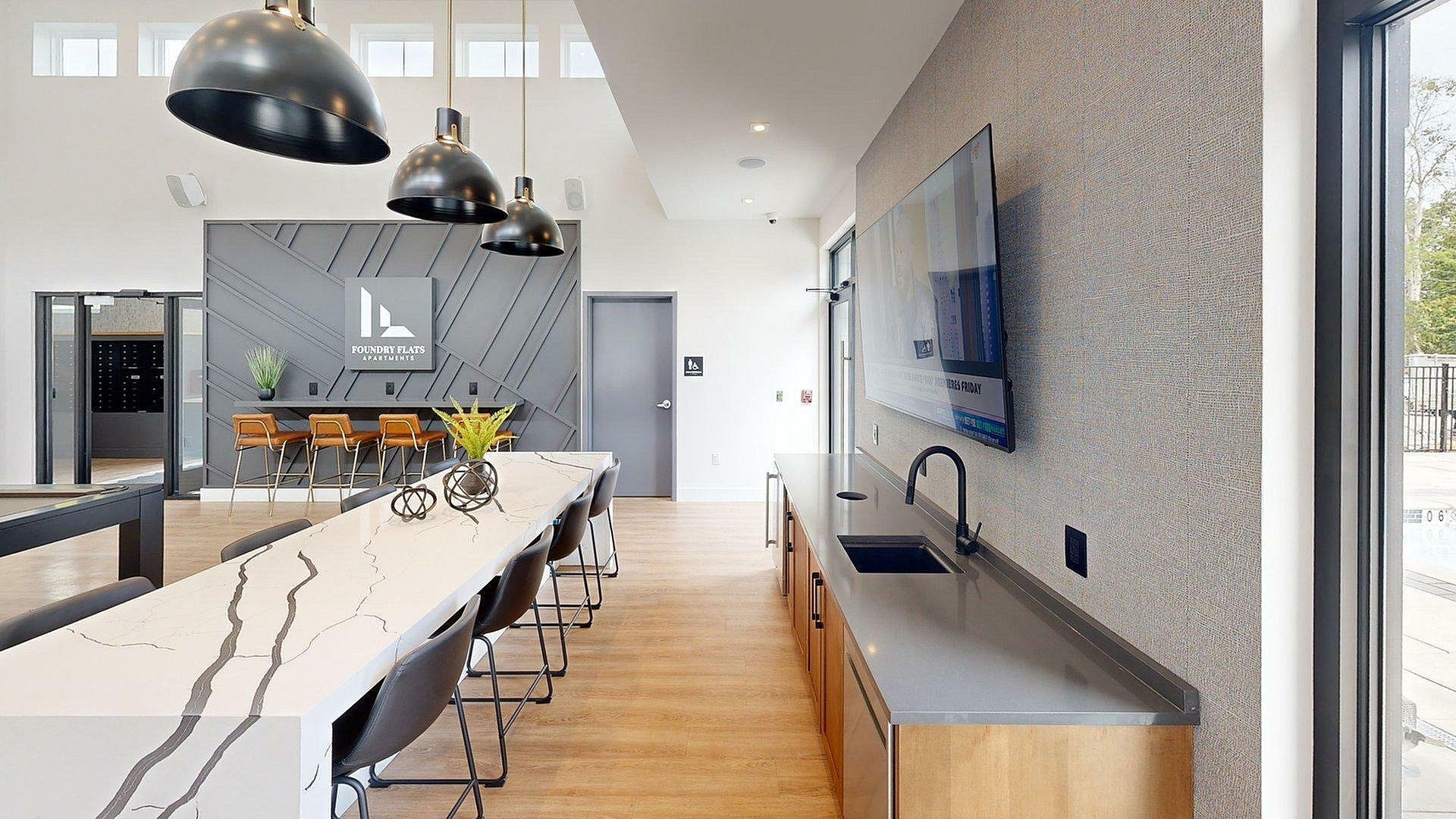 Modern and inviting community space at Foundry Flats Apartments with sleek lighting, a stylish bar area, and contemporary design elements.
