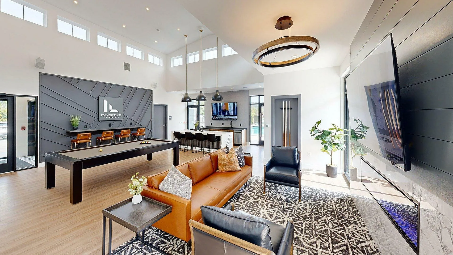 Luxurious and spacious apartment interior with modern decor, featuring a stylish leather sofa, chic black armchairs, elegant lighting, a large TV, and a sleek billiards table in an open-concept living area.