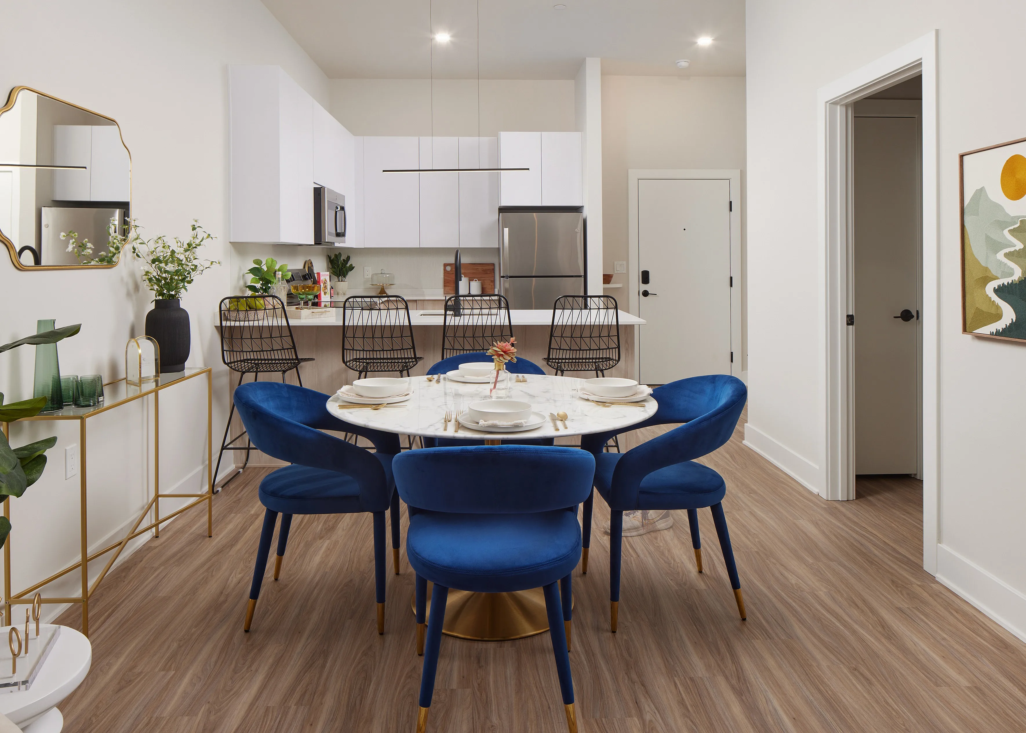 Chic apartment interior with a modern kitchen and dining area featuring blue velvet chairs, a marble table, and elegant decor.