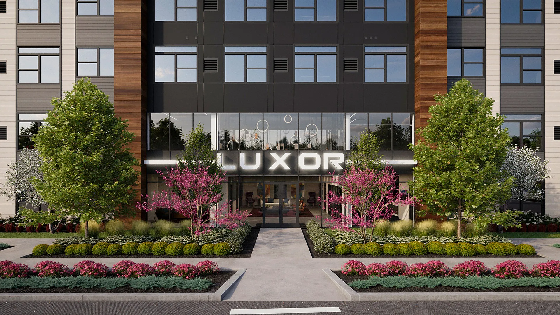 Modern apartment building entrance featuring sleek design, lush landscaping with vibrant pink blossoms, and tall green trees.