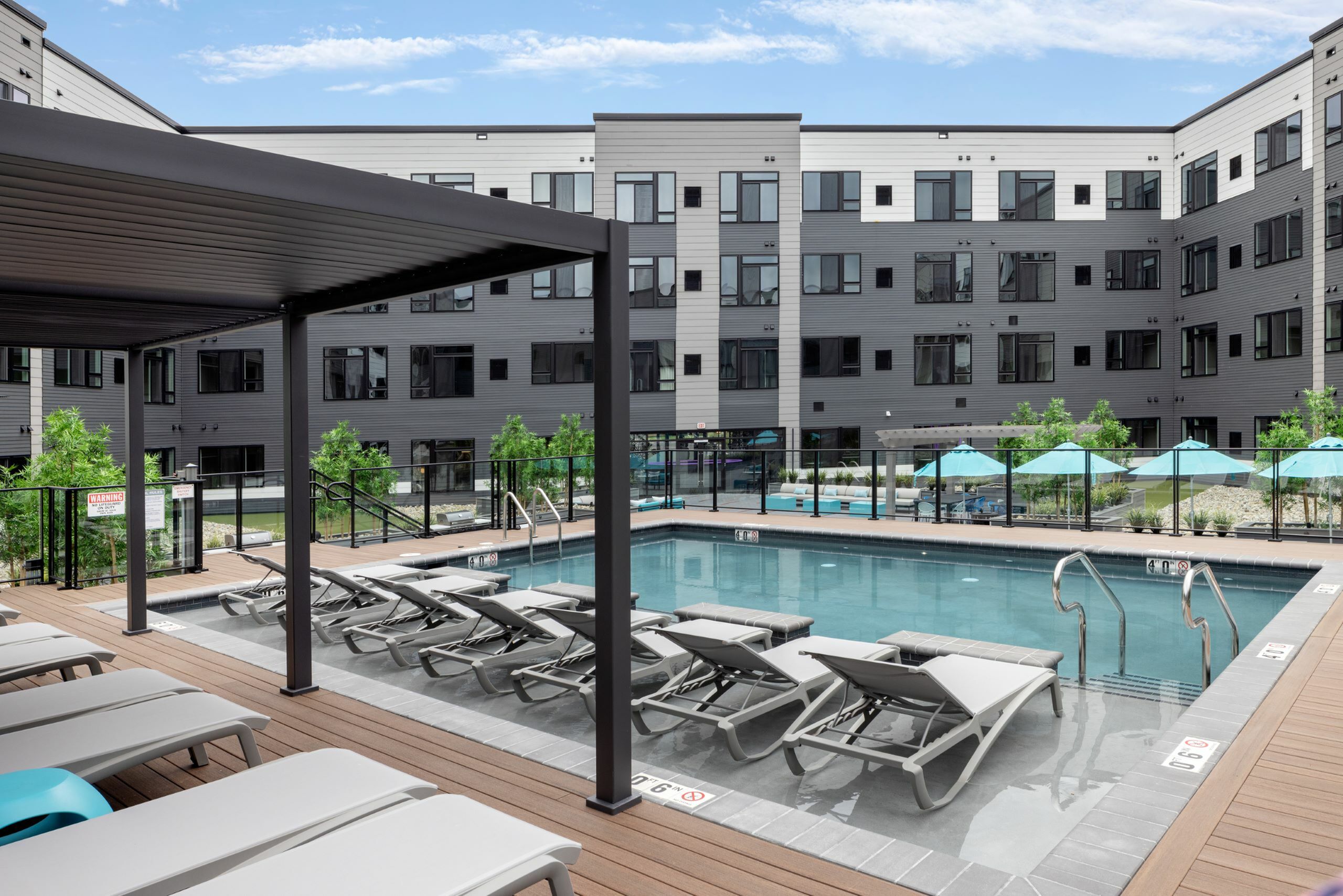 Inviting apartment complex courtyard featuring a sparkling swimming pool, modern lounge chairs, shaded pergola, and vibrant landscaping.