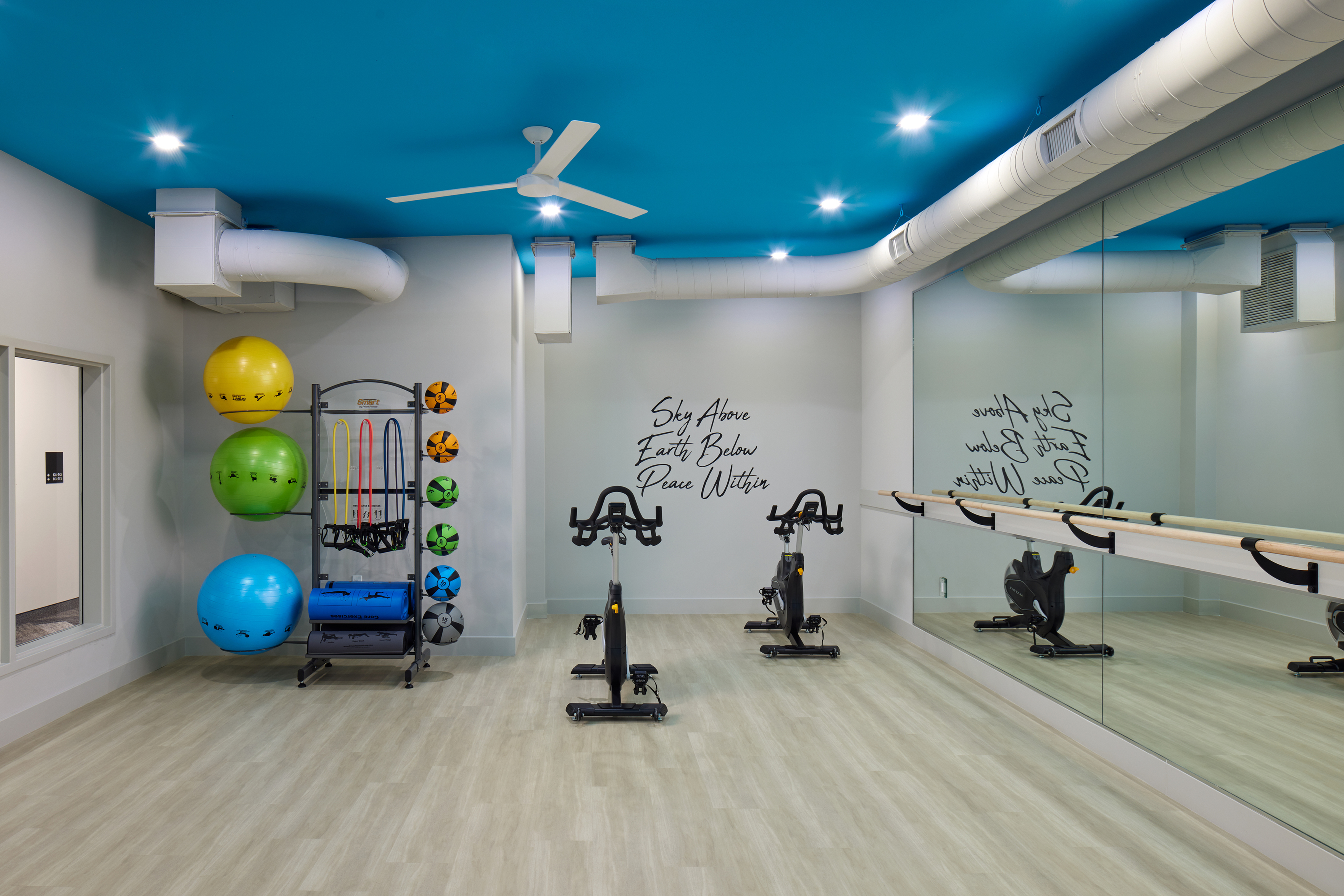 Modern fitness room with vibrant blue ceiling, exercise equipment, mirrored wall, and motivational quote for an inspiring workout environment.