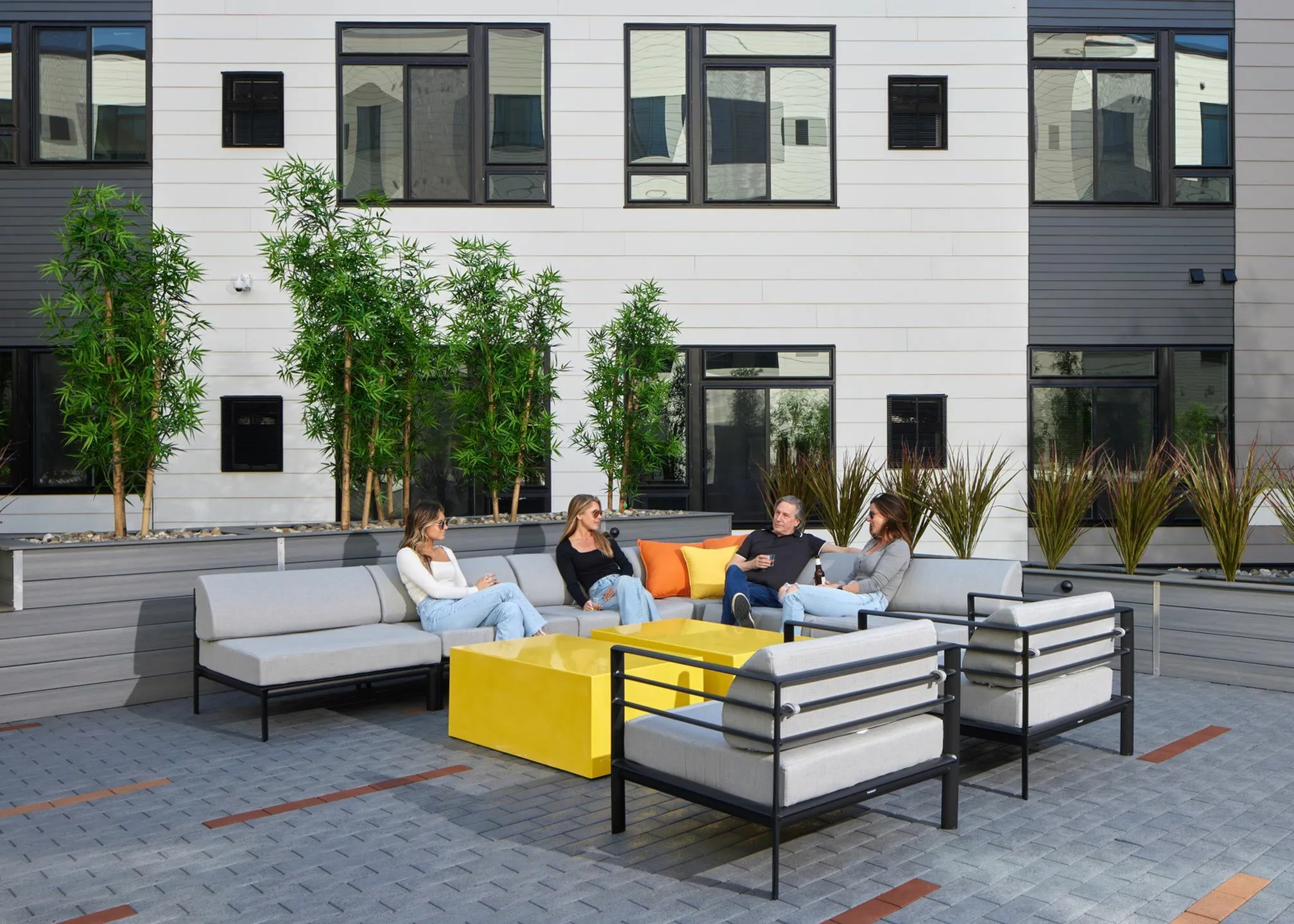 Modern outdoor courtyard with stylish seating, vibrant yellow tables, and lush greenery, offering a perfect spot for social gatherings.