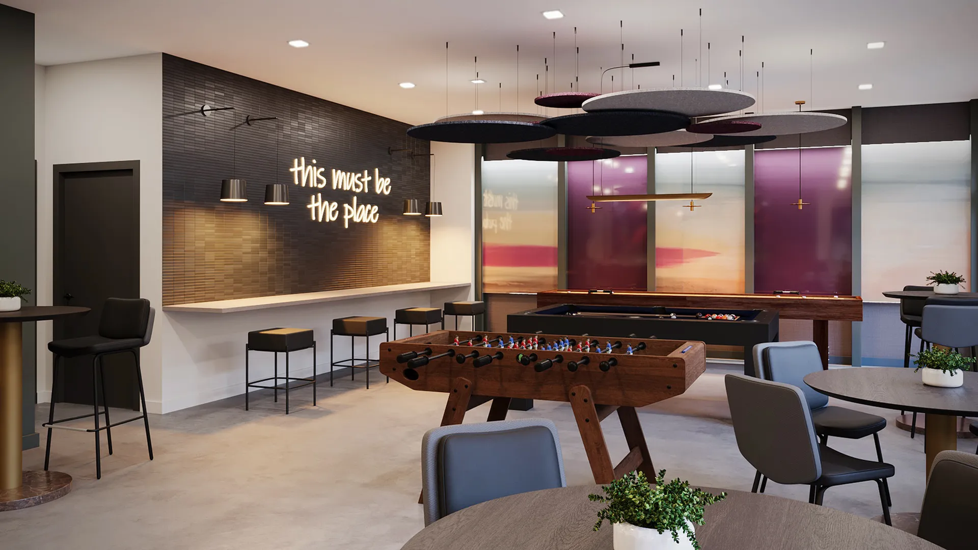 Vibrant communal lounge with chic decor, foosball table, and bar seating under modern lighting, perfect for social gatherings.