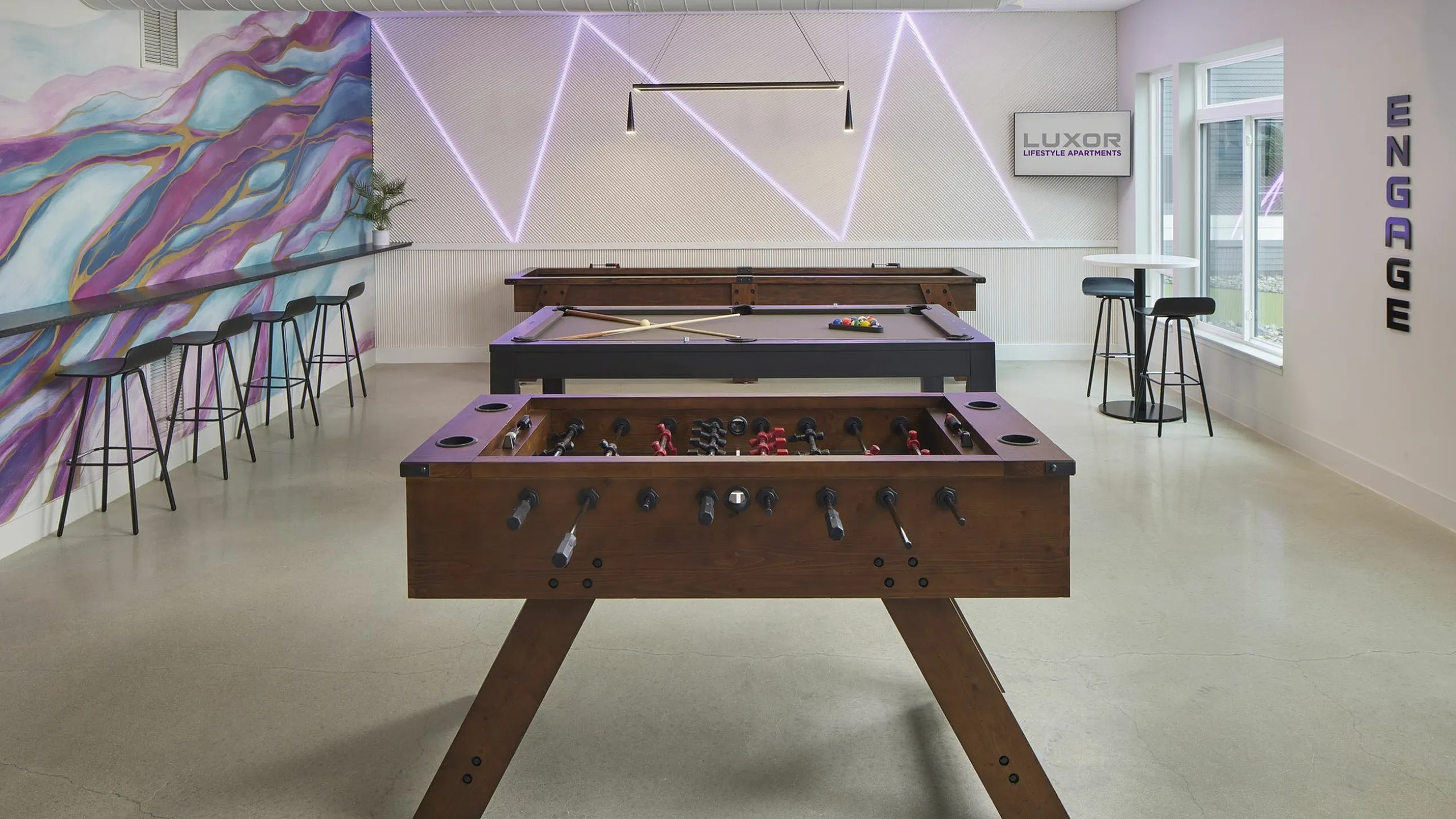 Vibrant game room with foosball and pool tables, contemporary seating, and colorful murals, perfect for entertainment at Luxor Lifestyle Apartments.