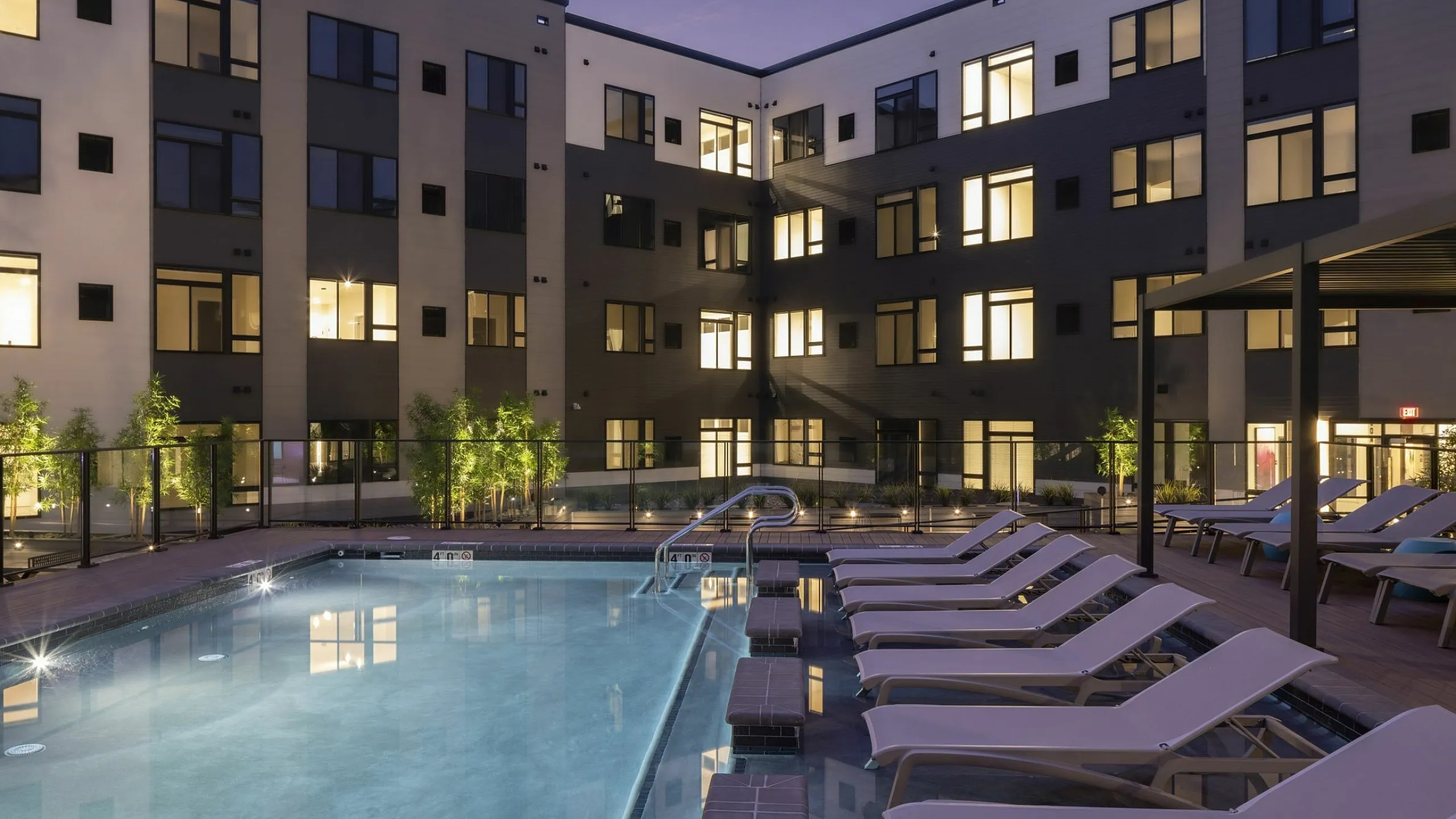 Elegant apartment complex at dusk with a glowing pool and inviting lounge chairs, perfect for relaxation and social gatherings.