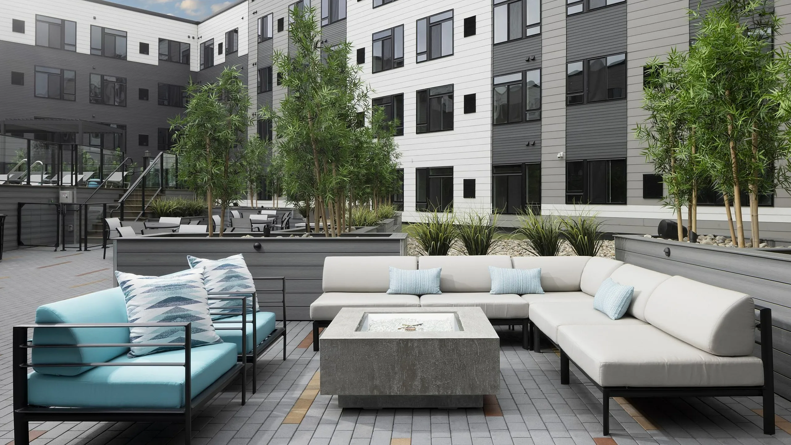 Modern apartment courtyard showcasing a stylish outdoor seating area with lush greenery and a sleek fire pit, ideal for relaxation and social gatherings.