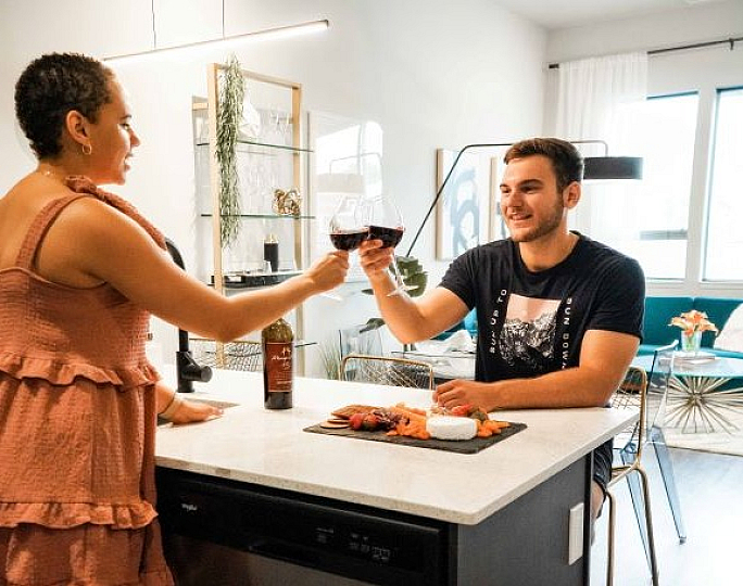 Modern kitchen with a warm ambiance featuring a couple enjoying wine and appetizers at the island, with stylish living area in view.